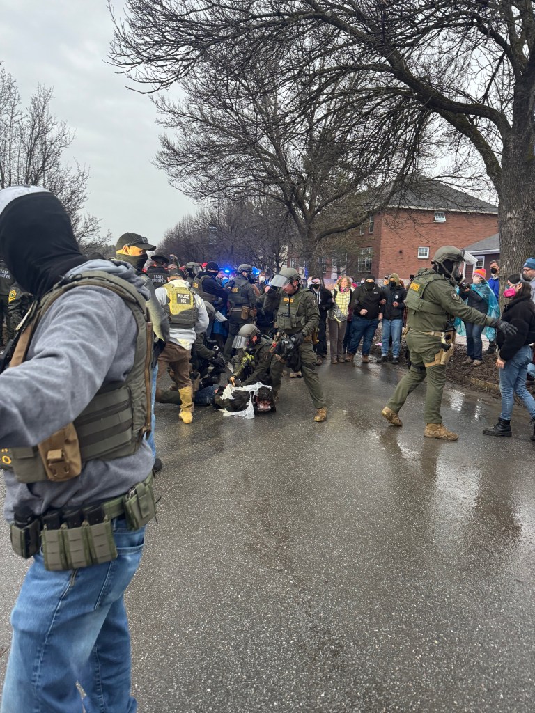 State police handcuff a community member who is face down on the ground in the street